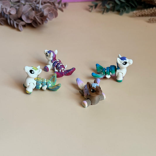 Four small mermaid unicorn 3d printed figurines on a beige surface with a blurred background