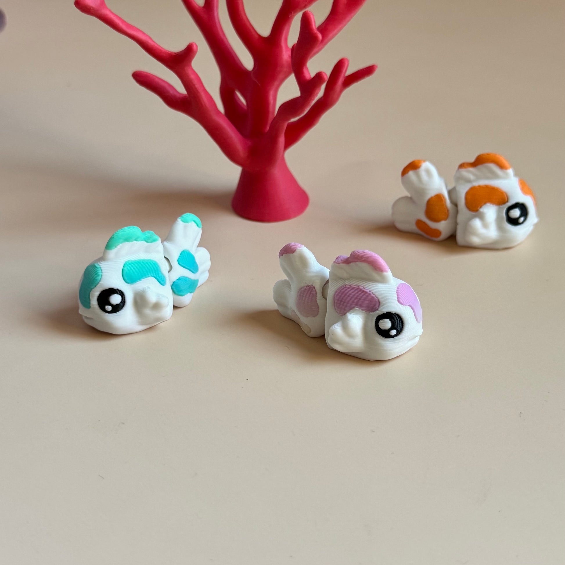 Three mini 3d printed koi fish with colourful markings on a beige surface, with a beige background.