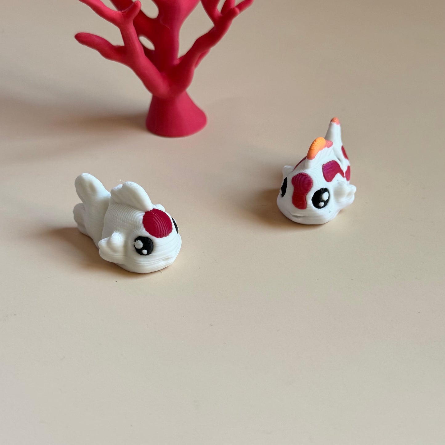 Two 3d printed mini fish figurines with red and black markings on a beige surface.