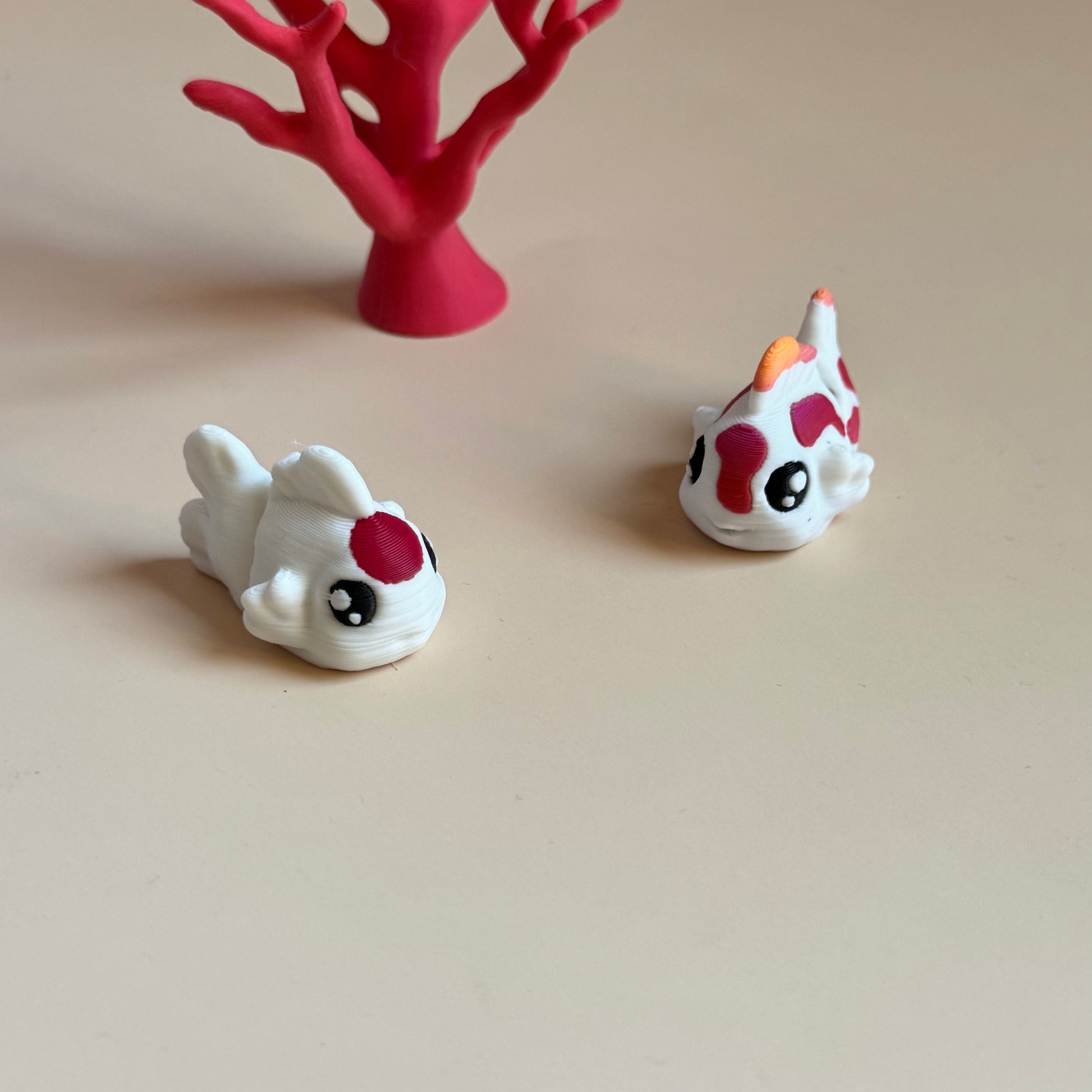 Two 3d printed mini fish figurines with red and black markings on a beige surface.
