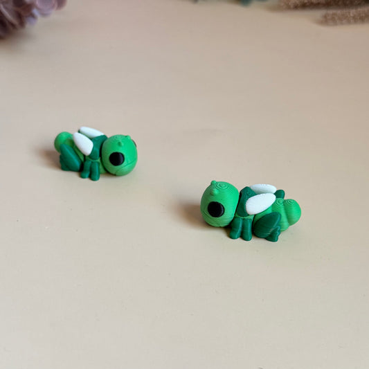 Two green 3d printed mini grasshopper figures on a beige surface