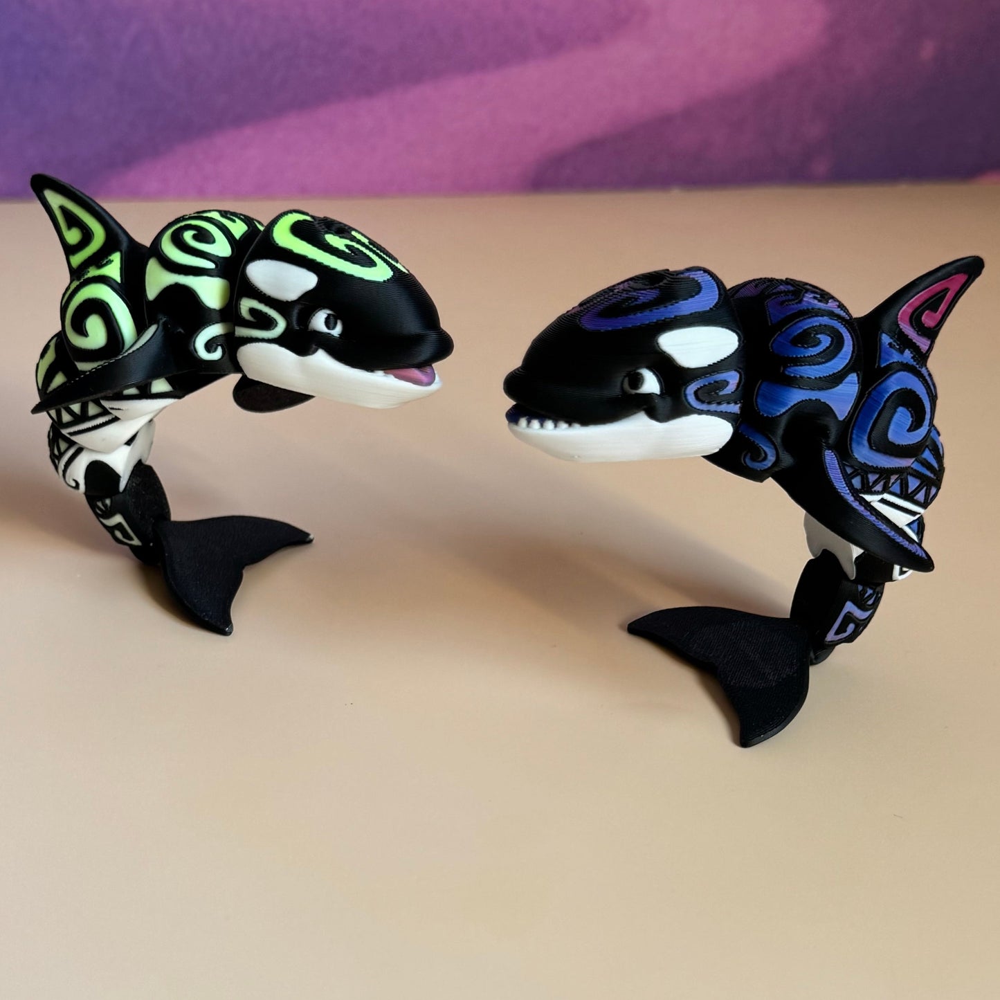 Two orca figurines with colorful designs on a beige surface.